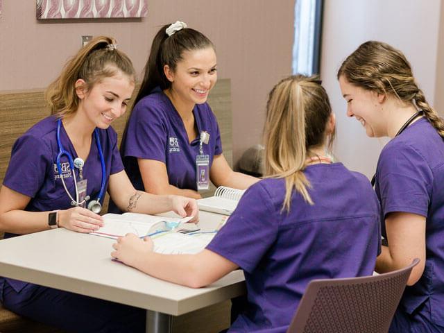 SBU students smiling as they study at a table